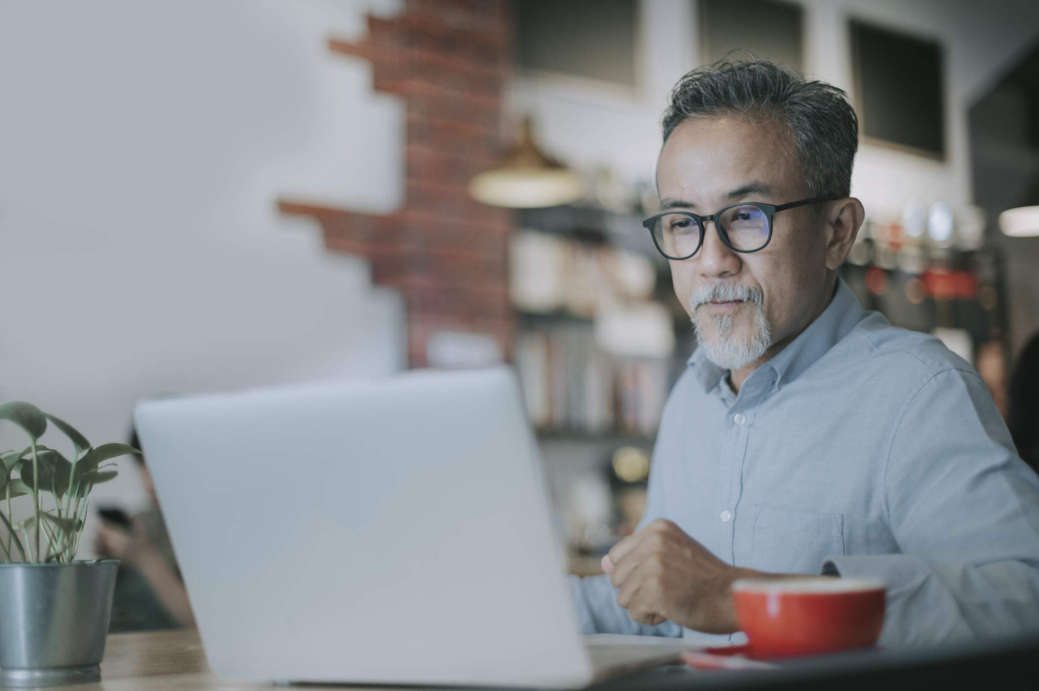 an asian chinese senior man having discussion with his colleague via online virtual meeting in a cafe